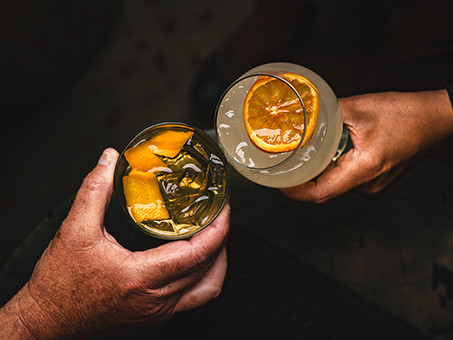 Two people toasting cocktails with an orange zest garnish